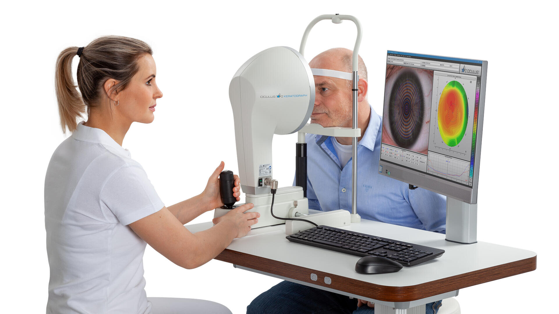 Eine Optometristin bedient ein Augenuntersuchungsgerät, während ein älterer Mann sein Kinn auf das Gerät stützt und sich einem Augenscan unterzieht. Ein Monitor zeigt die Ergebnisse des topografischen Augenscans in Farbe an.