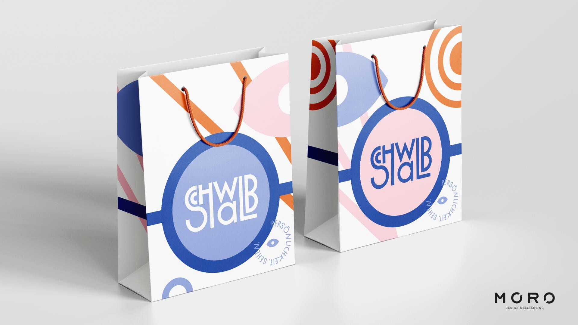Zwei farbenfrohe Einkaufstaschen mit abstrakten geometrischen Mustern in Blau, Orange und Rot. Die Taschen zeigen einen auffälligen blauen Kreis mit stilisiertem weiß-blauem Text im Inneren. Das Logo von MGRO Design & Marketing erscheint in der unteren rechten Ecke.