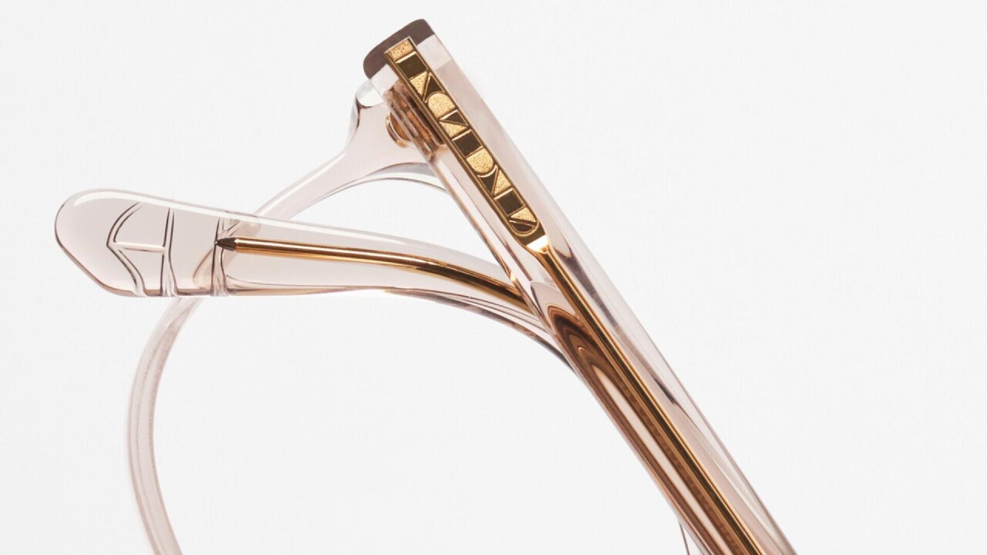 Close-up of translucent, light brown eyeglass frames with gold PRADA branding on the arm, set against a plain white background.
