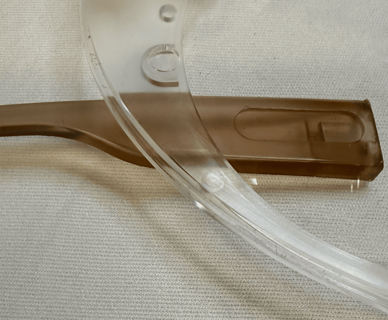 Close-up of a transparent plastic visor overlapping a brown plastic handle; both rest on a light-colored, textured fabric surface.