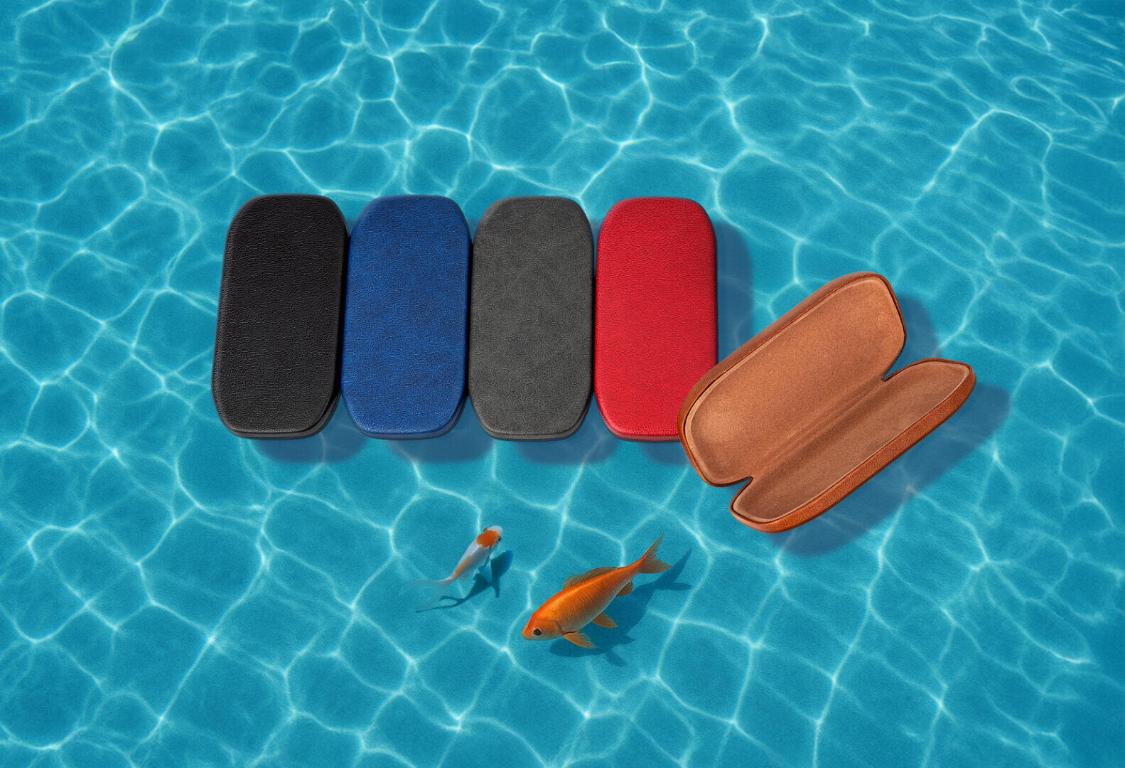 Fünf rechteckige Brillenetuis in Schwarz, Blau, Grau, Rot und Hellbraun sind auf einer blauen, sonnenbeschienenen Poolfläche angeordnet. Das hellbraune Etui ist geöffnet, und zwei Goldfische schwimmen in der Nähe.