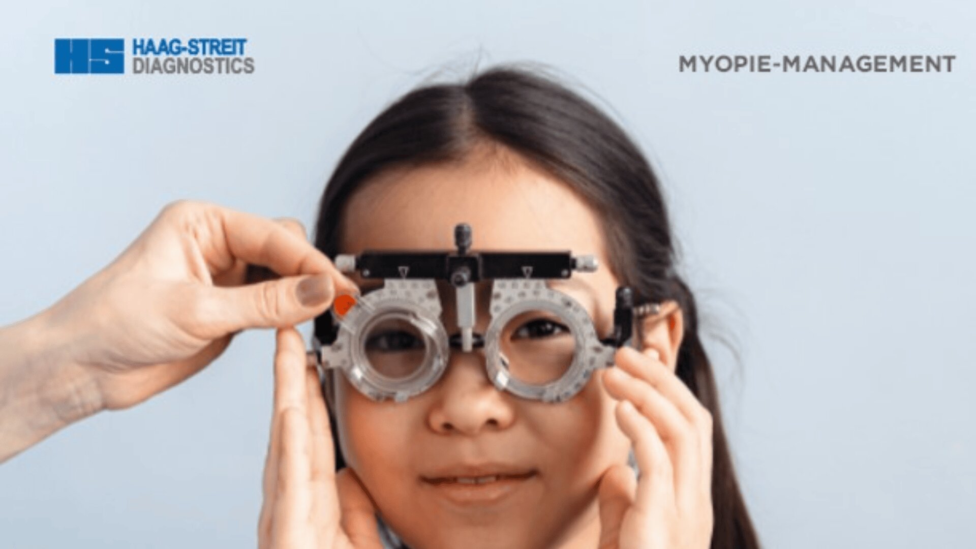 Ein junges Mädchen lächelt, während es bei einer Augenuntersuchung einen Phoropter trägt. Die Hand eines Fachmanns justiert das Gerät. Der Text lautet "HAAG-STREIT DIAGNOSTICS" und "MYOPIE-MANAGEMENT" auf hellblauem Hintergrund.