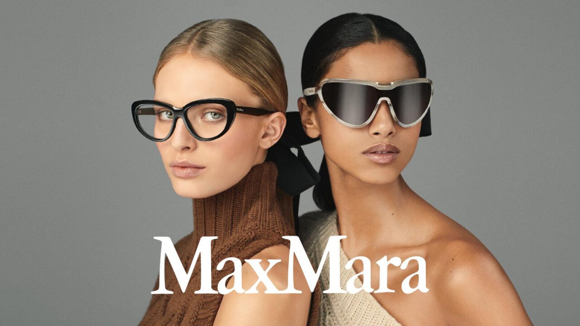 Two women pose side by side wearing stylish sunglasses and sleeveless knit tops against a gray background. The MaxMara logo appears in white text at the bottom of the image.