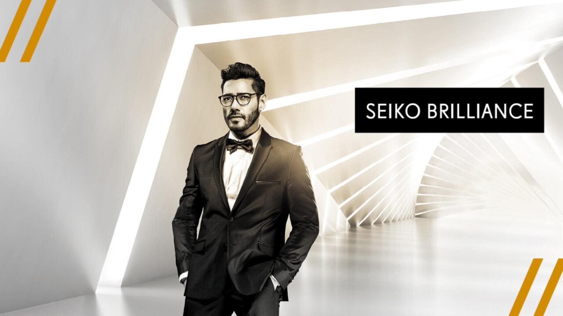 A man in a black tuxedo stands confidently in a futuristic, white geometric hallway. The text SEIKO BRILLIANCE appears beside him. The overall design is modern and sleek.