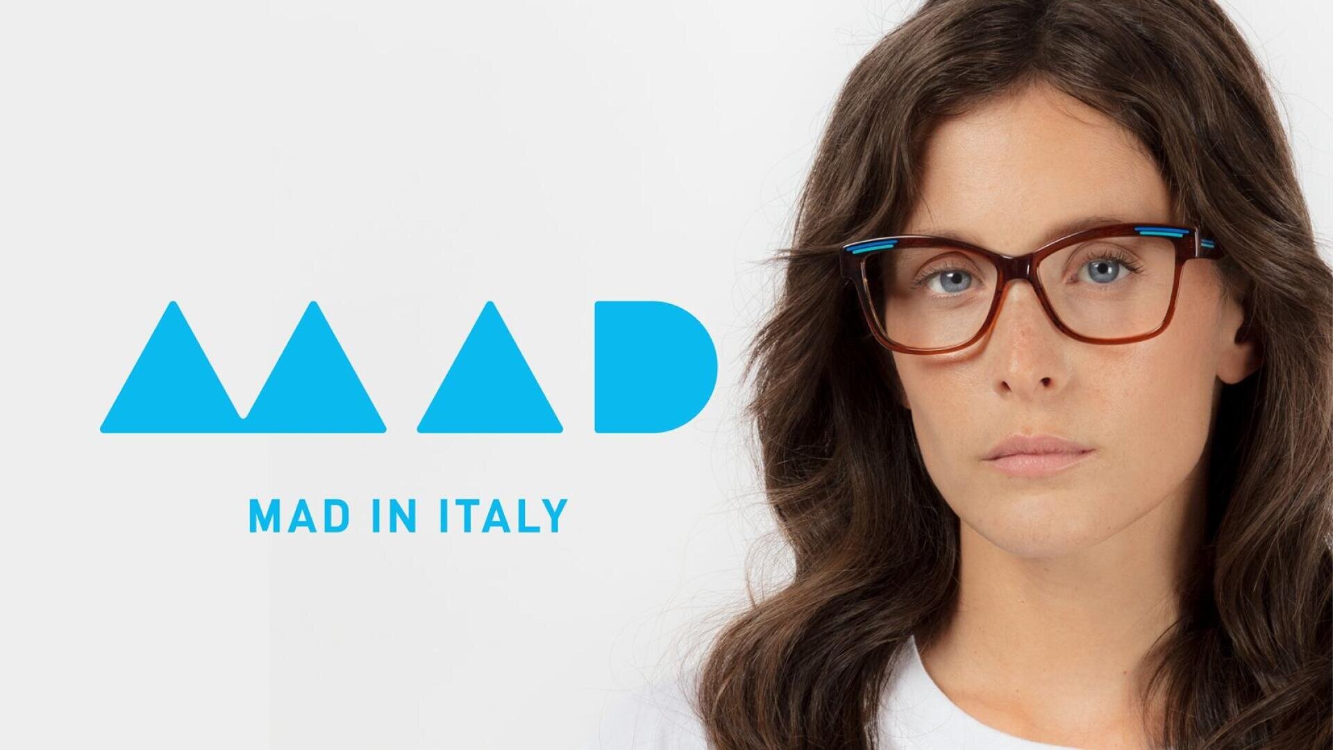 A woman with long brown hair and glasses looks at the camera. To her left, blue geometric shapes spell MAD, with the text MAD IN ITALY below, all on a white background.
