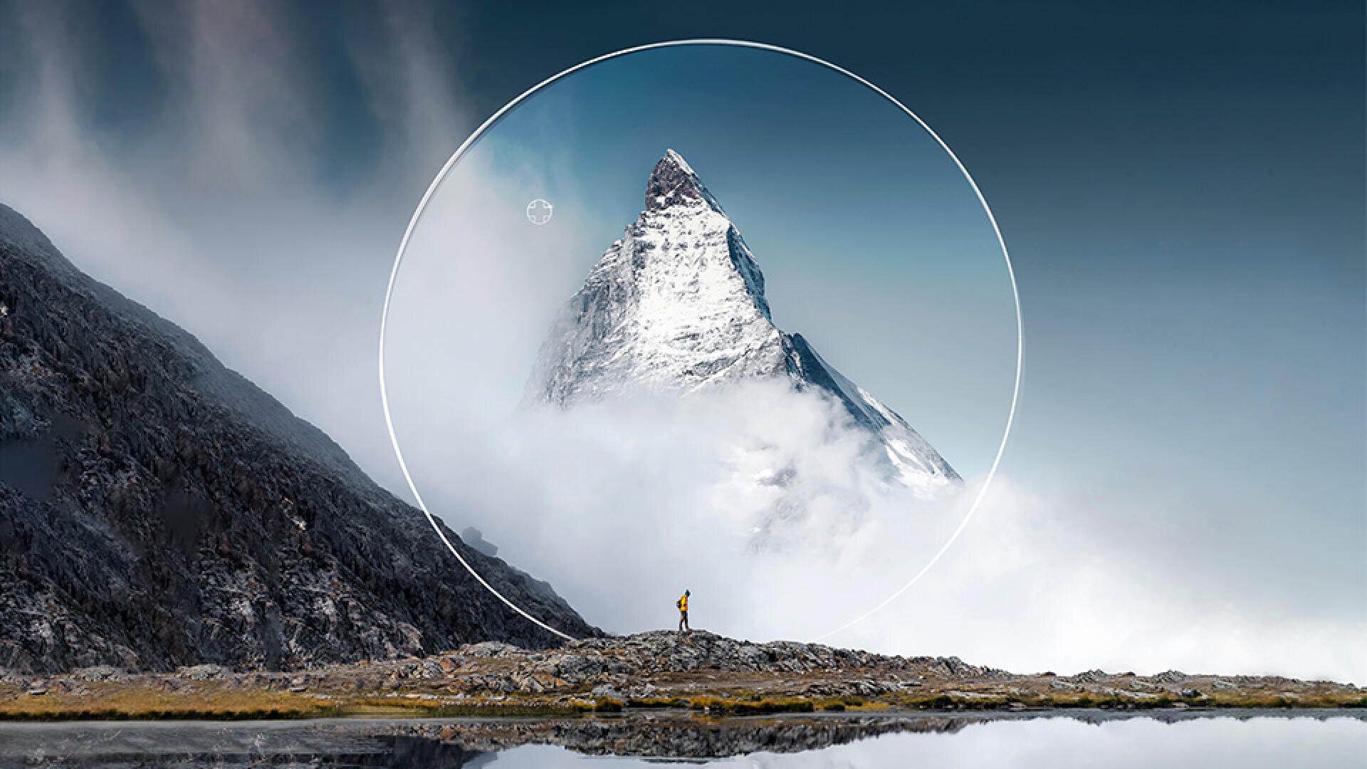 A lone person stands on rocky ground and looks at a snow-covered mountain peak surrounded by fog. A white circle is digitally superimposed around the peak against a clear, dark sky.