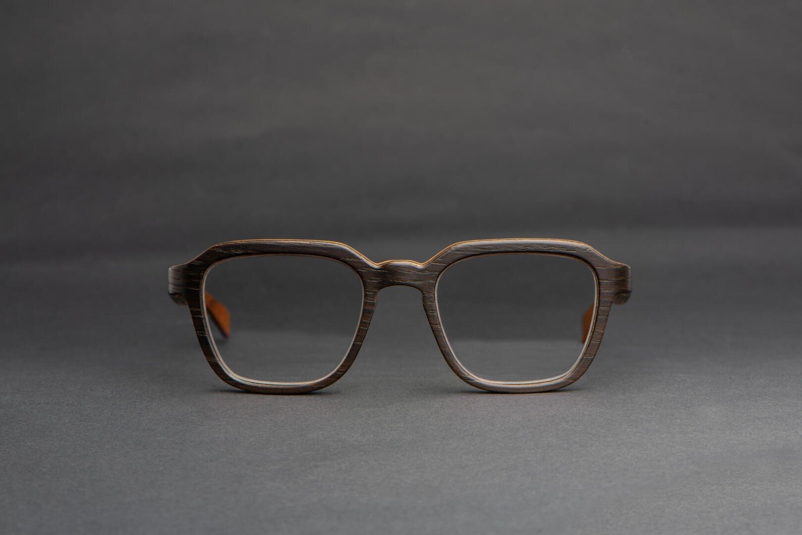 A pair of eyeglasses with dark, wood-textured rectangular frames is displayed against a plain, dark gray background.