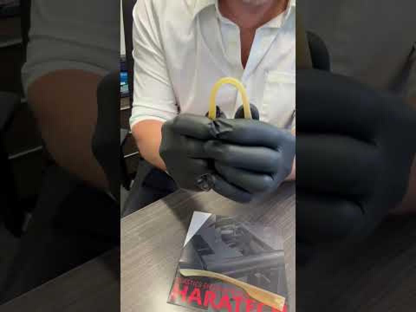 A person wearing a white shirt and black gloves is holding a yellow rubber dam. On the desk in front of them is a brochure entitled MARALEE.