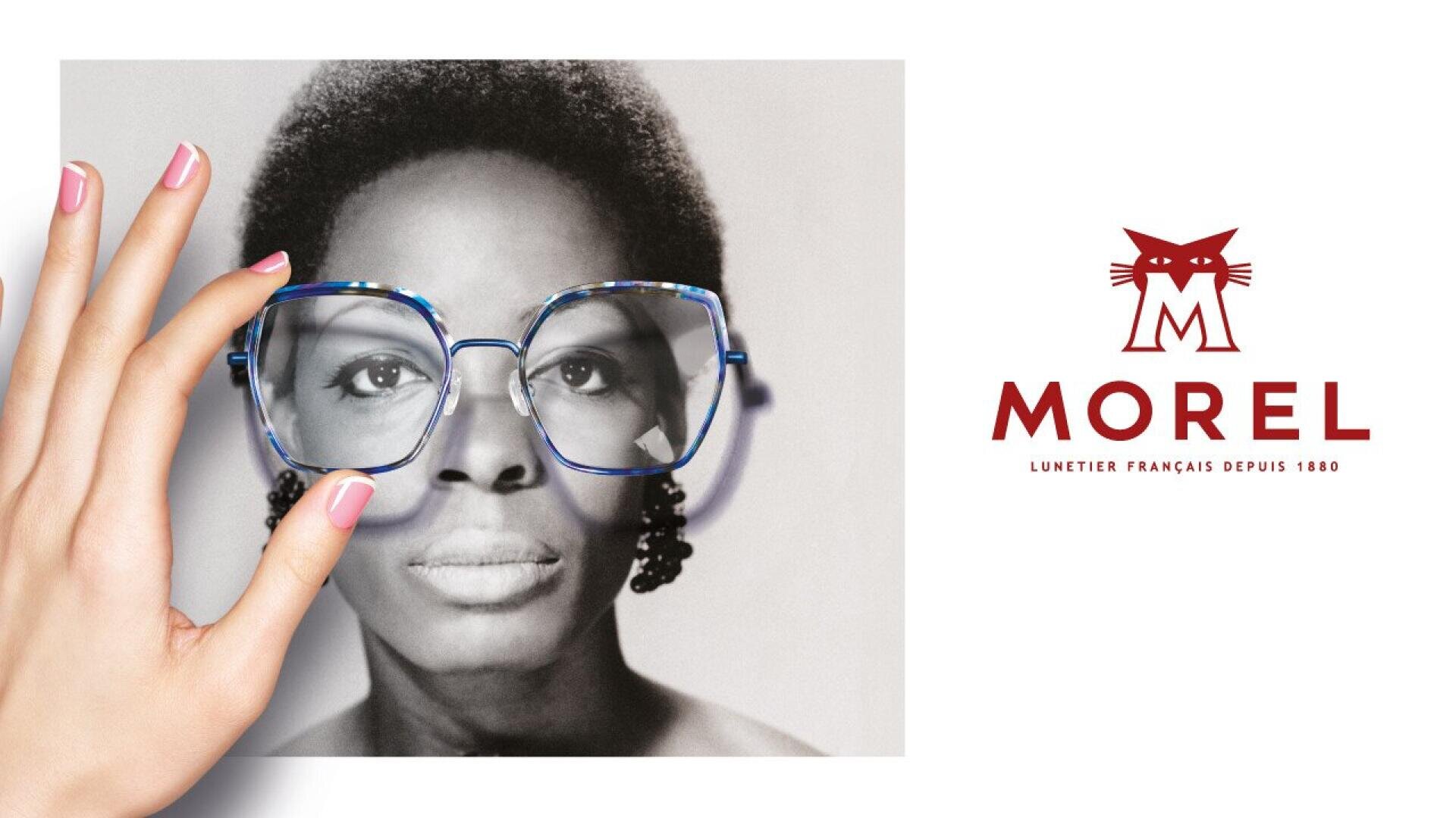 A hand holds a black-and-white photo of a woman, aligning oversized blue glasses over her eyes. To the right, the Morel logo with a stylized cat and the text Lunetier Français Depuis 1880 is displayed.
