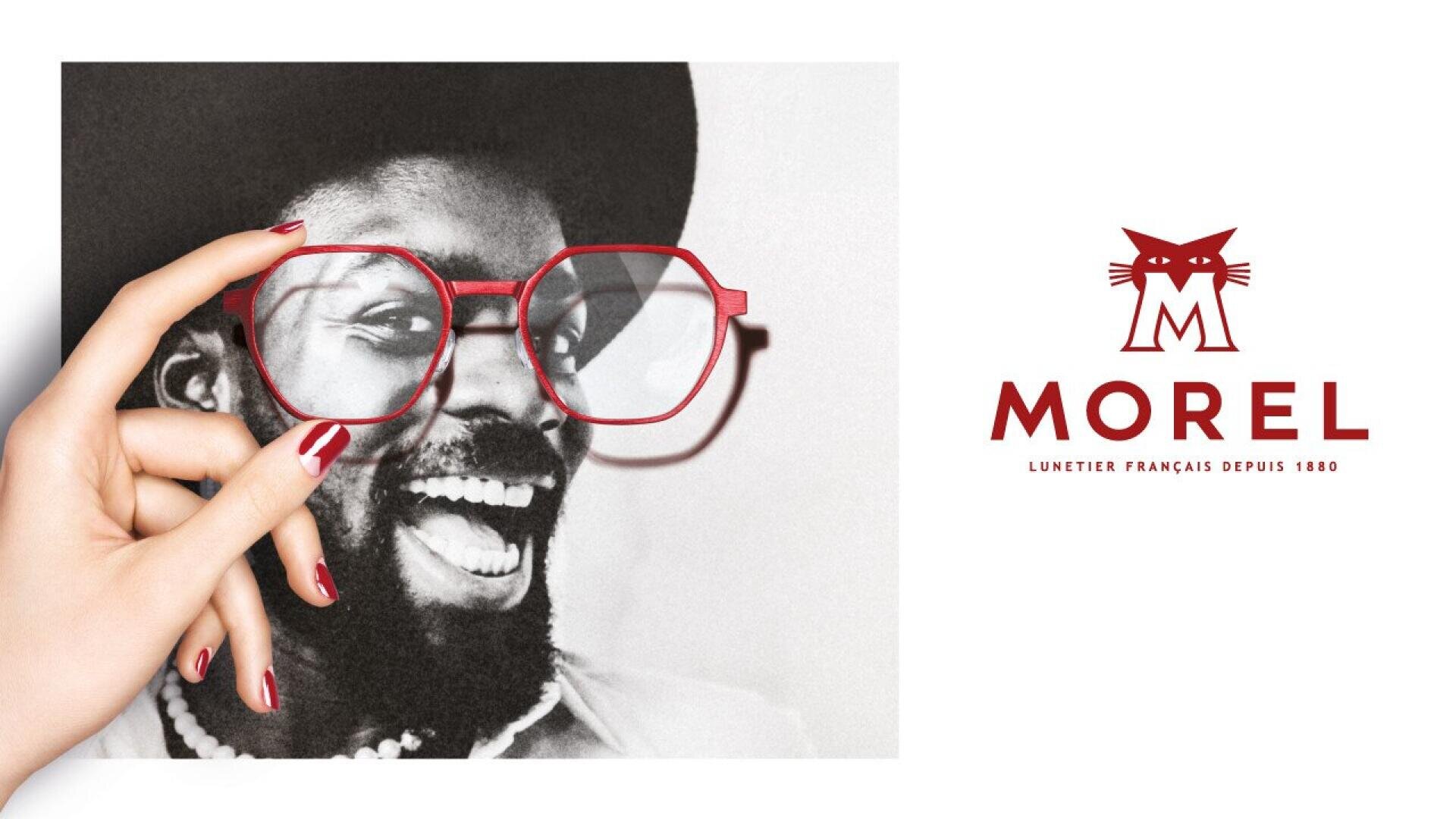 A hand with red nail polish holds red eyeglasses over a black-and-white photo of a smiling man, matching the Morel logo featuring a stylized cat and text on the right side.