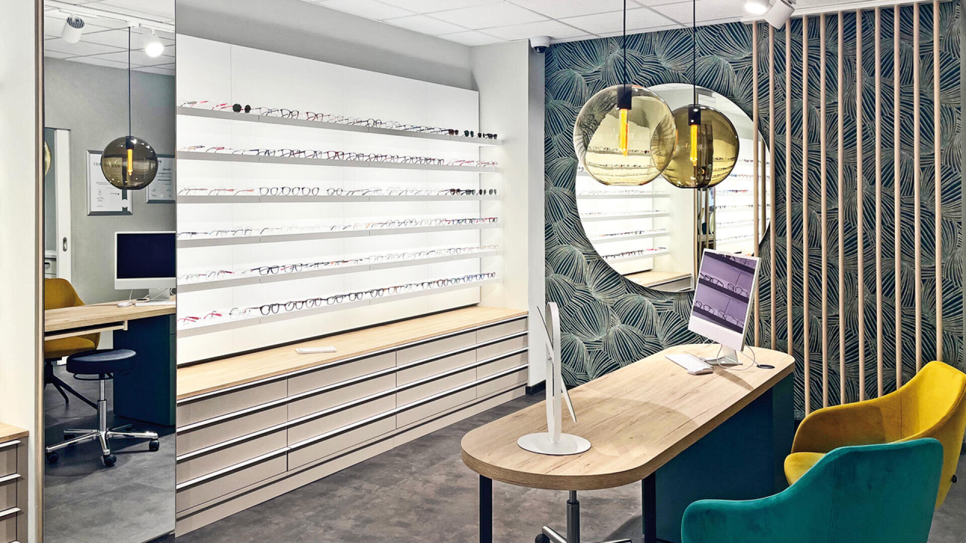 Eine moderne Optikerpraxis mit Brillenregalen, einem eleganten Schreibtisch mit Computer, gelben und grünen Stühlen, gemusterter Tapete und großen runden Spiegeln an der Wand.