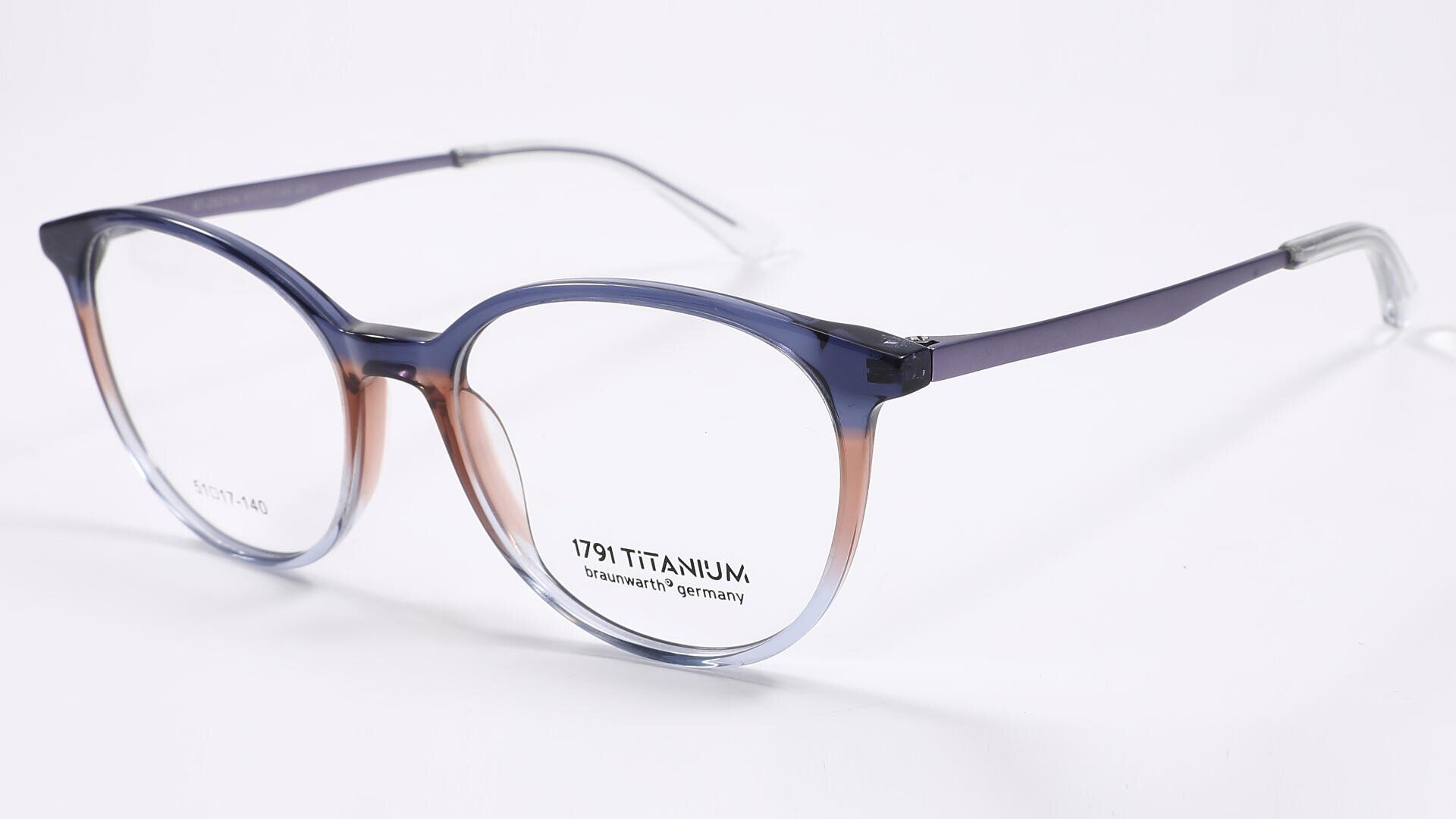 Eine runde Brille aus Titan mit einem Farbverlaufsrahmen, der von oben blau zu unten klar übergeht, auf weißem Hintergrund.