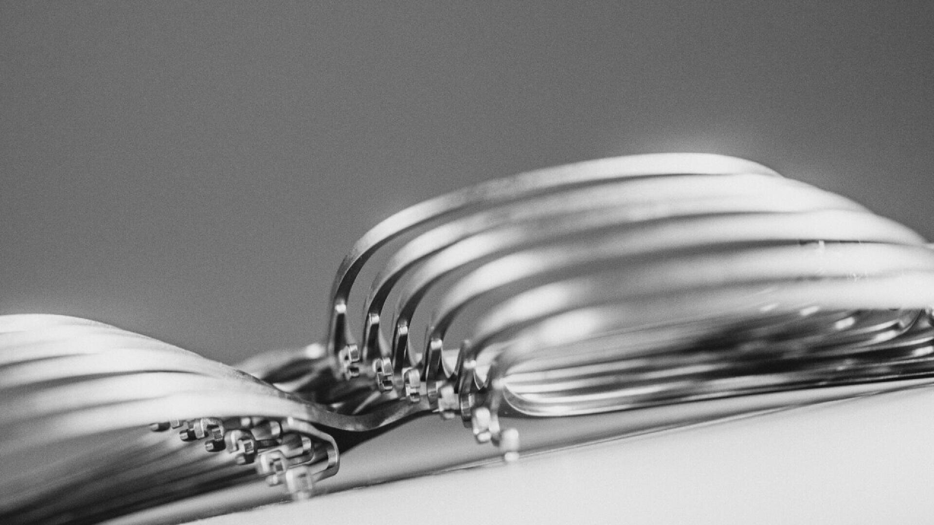 Close-up, black-and-white image of several metal forks stacked together, showing their curved tines overlapping and creating a pattern against a blurred background.