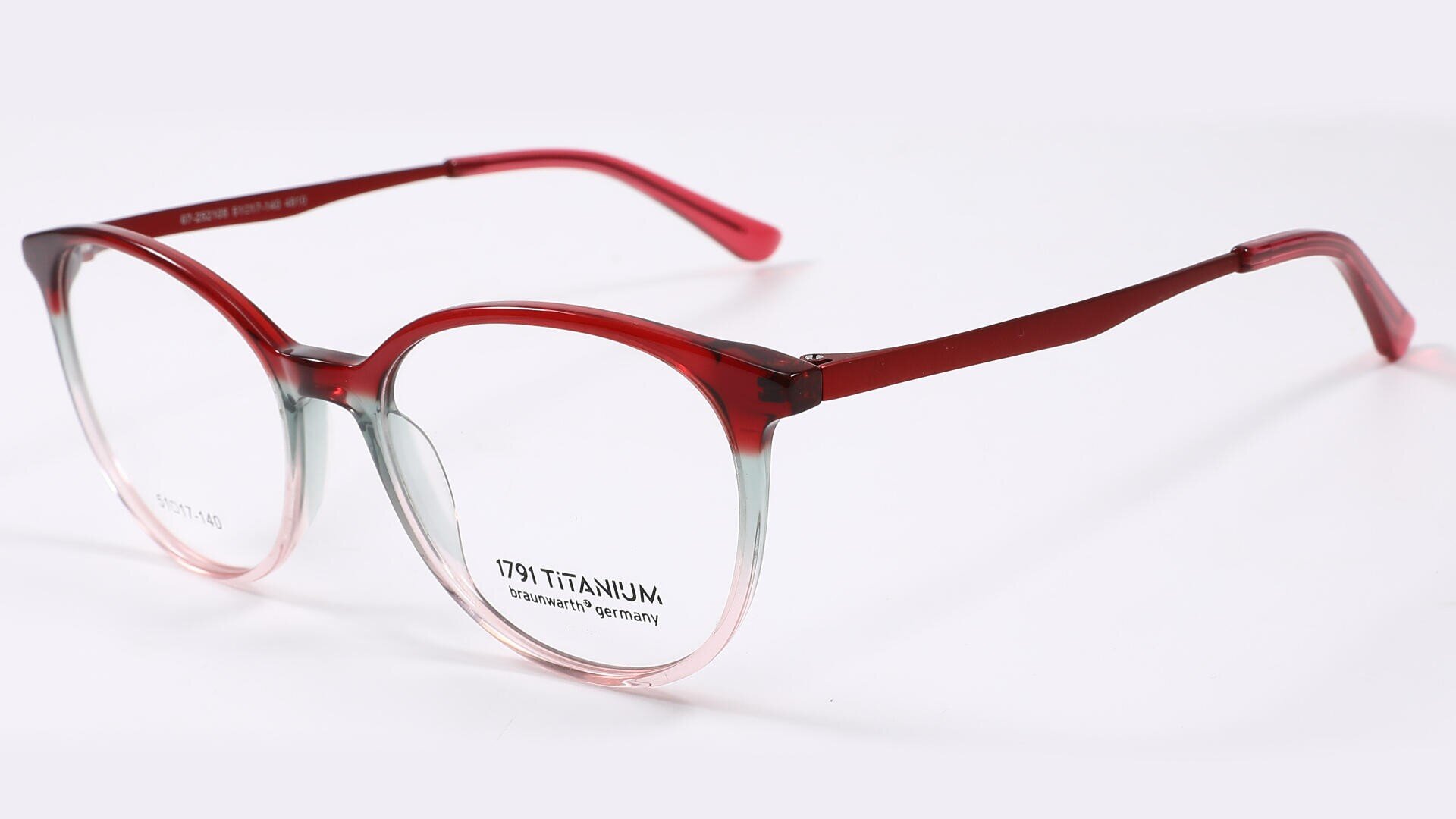 Eine runde Brille mit rotem Rahmen, der nach unten hin klar wird, auf weißem Hintergrund. Die Bügel sind durchgehend rot, und auf einem Glas und der Innenseite des Bügels ist Text sichtbar.