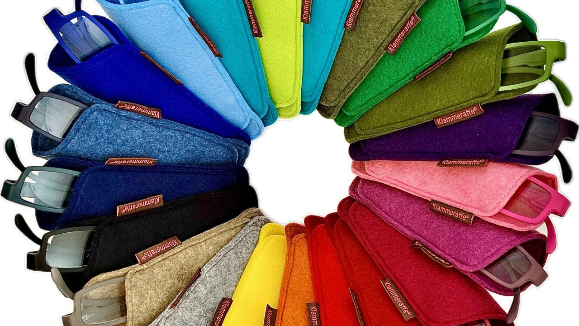 A semicircle of eyeglasses in colorful felt cases arranged by color gradient, from blue and green to red and yellow, with the brand name “Klammeraffe” on each case. The glasses arms are partially visible.