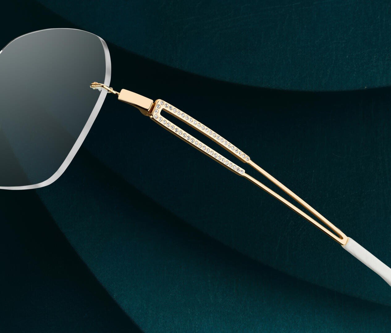 Close-up of a pair of glasses with gold and diamond-studded temples against a dark green, textured background. The image highlights the luxurious details and craftsmanship of the frame.