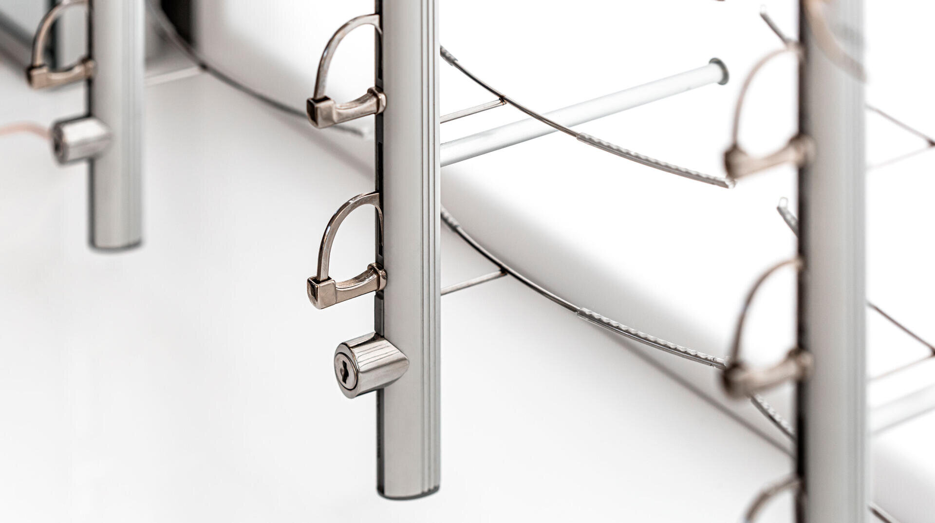 Nahaufnahme von Metallstangen mit Schlössern und Kabeln, Teil eines Sicherheits- oder Schließsystems, auf weißem Hintergrund. Das Bild betont metallische Texturen und sauberes, modernes Design.