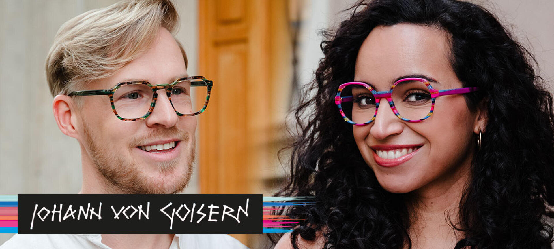 Ein lächelnder Mann und eine lächelnde Frau tragen bunte, modische Brillen; die Brille des Mannes ist grün gemustert, die der Frau rosa mit Streifen. „Johann von Goisern“ steht über einem Grafikstreifen unten links.