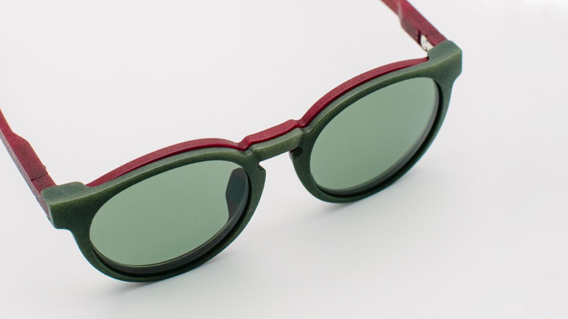 Round sunglasses with green lenses and a two-tone frame featuring dark green around the lenses and burgundy red along the arms and bridge, set against a plain white background.