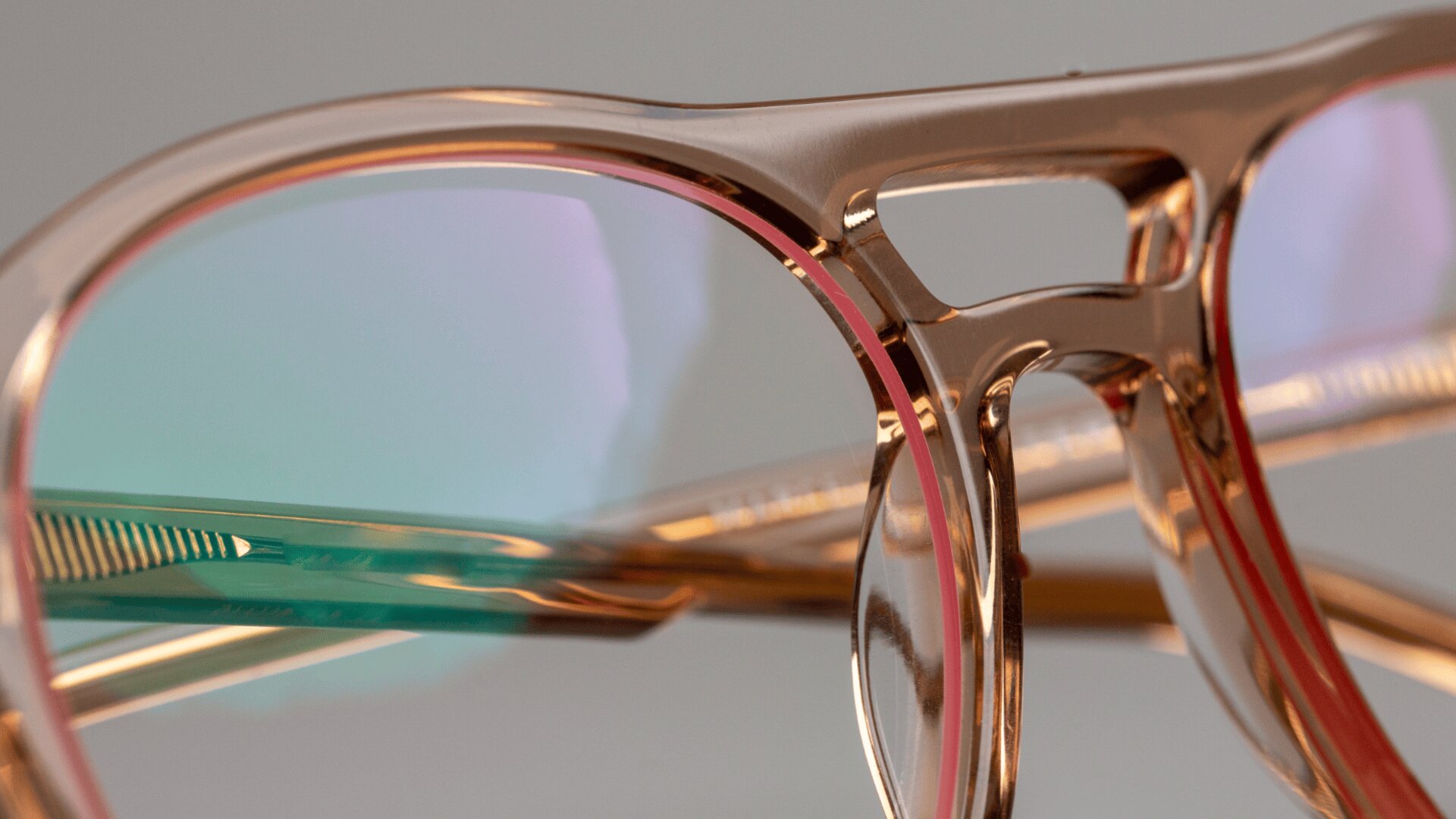 Nahaufnahme einer stilvollen Brille mit einem durchscheinenden, roségoldenen Rahmen und leicht getönten Gläsern, die das Licht reflektieren und auf dem Glas subtile grüne und violette Farbtöne erzeugen.