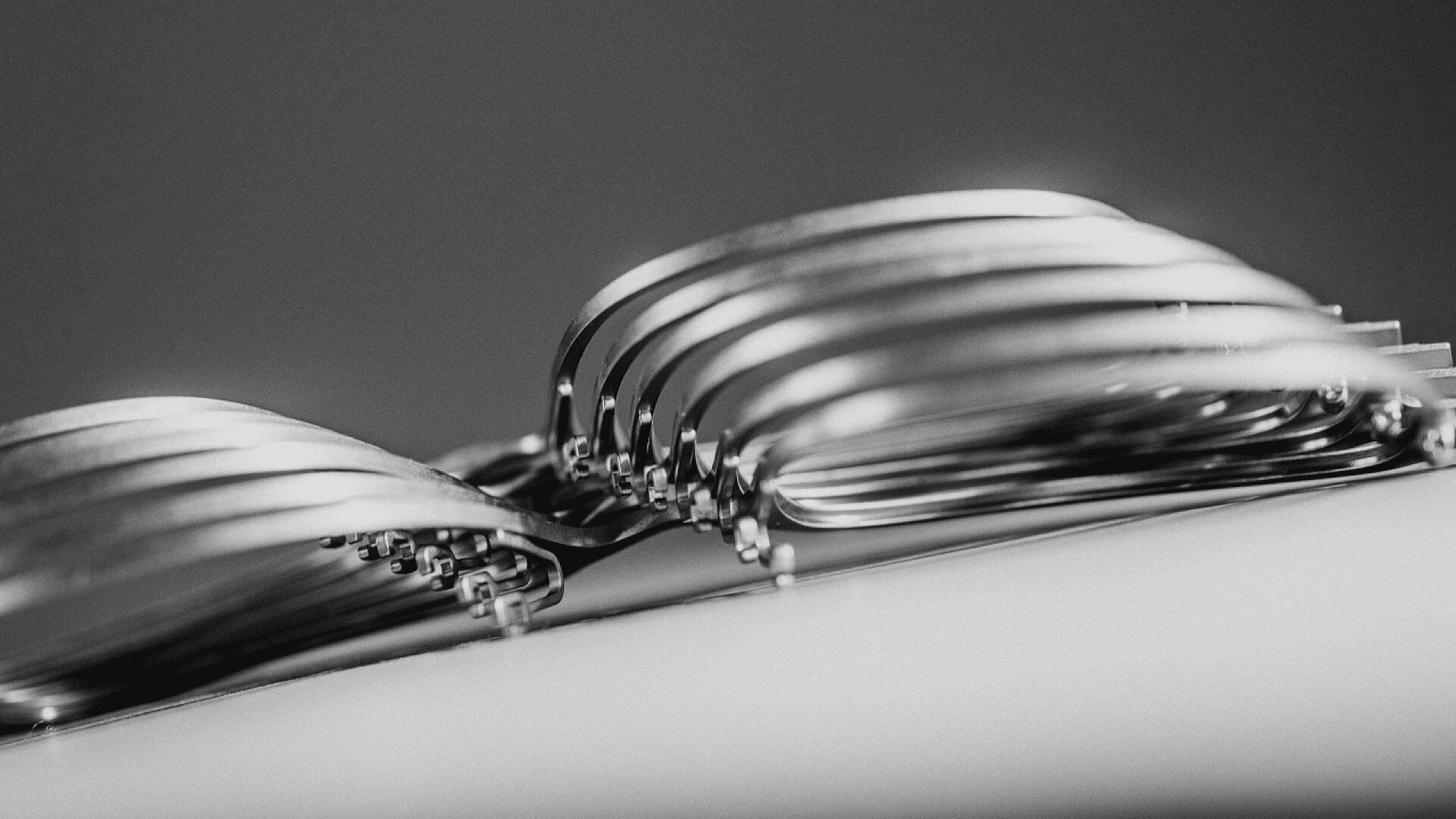 Eine Nahaufnahme in Schwarz-Weiß von mehreren aufeinander gestapelten Metallgabeln, die ihre gebogenen Zinken und Griffe in einer abstrakten Schichtung zeigen.