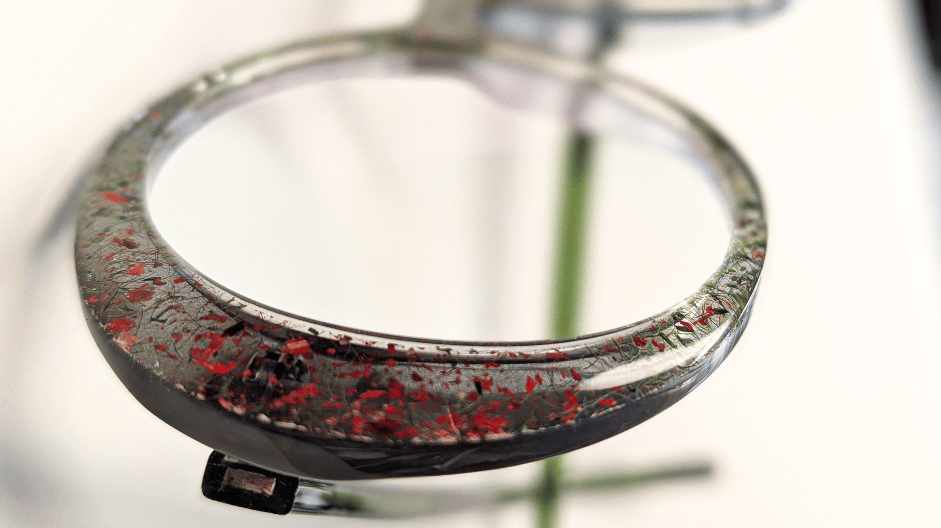 Nahaufnahme einer Brille mit runden Gläsern; der Rahmen weist zu den Rändern hin ein gesprenkeltes Muster aus Rot und Schwarz auf, und der Hintergrund ist sanft verschwommen.