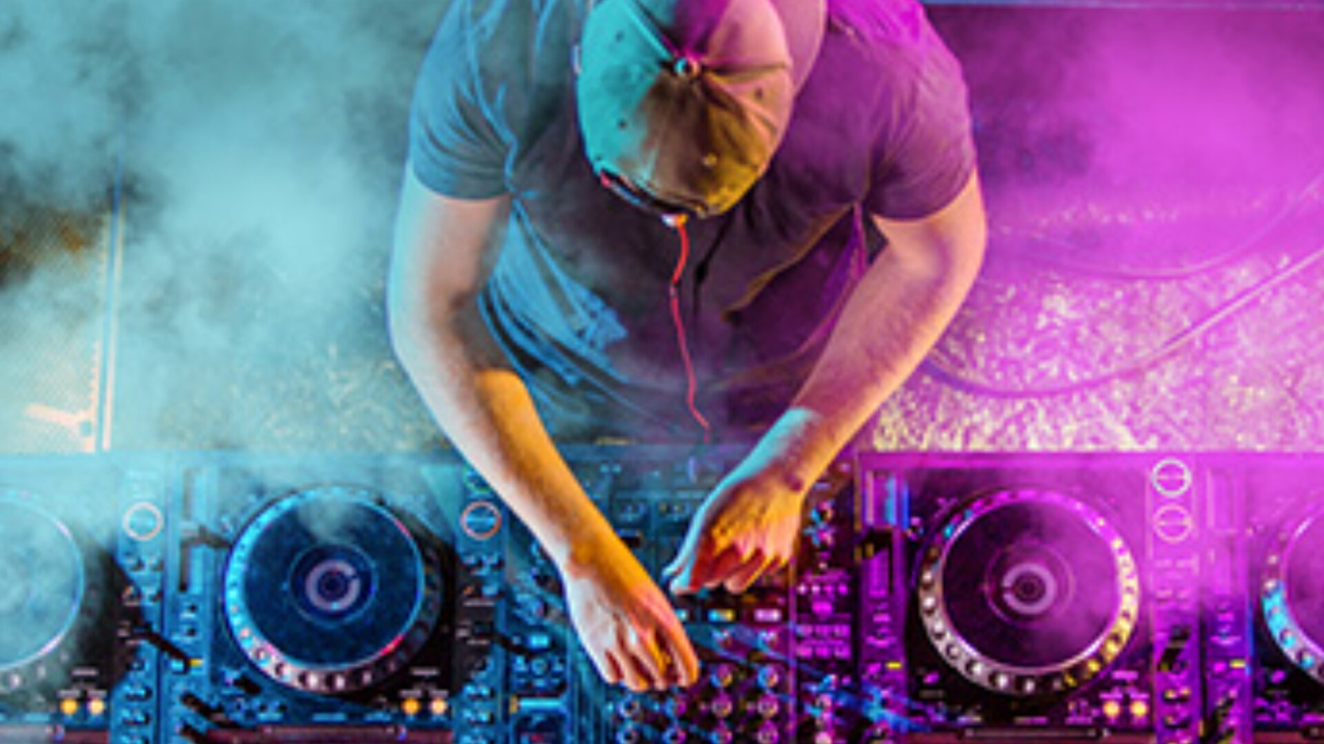 Ein DJ mit Mütze steht an einem Mischpult, umgeben von bunten Lichtern und Rauch, von oben gesehen.