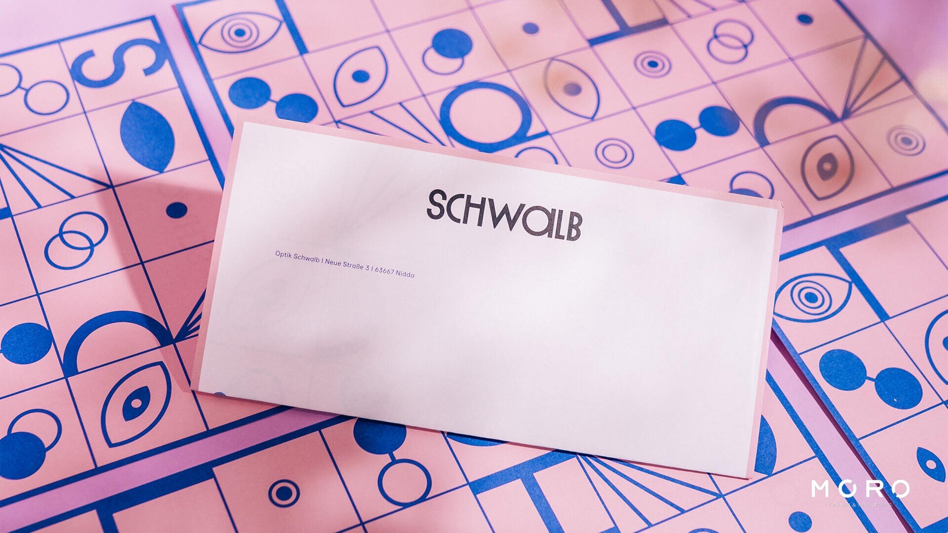 Ein weißer Umschlag mit der Aufschrift „SCHWALB“ liegt auf einer rosa und blau gemusterten Oberfläche mit geometrischen und augenähnlichen Formen; in der unteren rechten Ecke steht in weißer Schrift „MURO“.