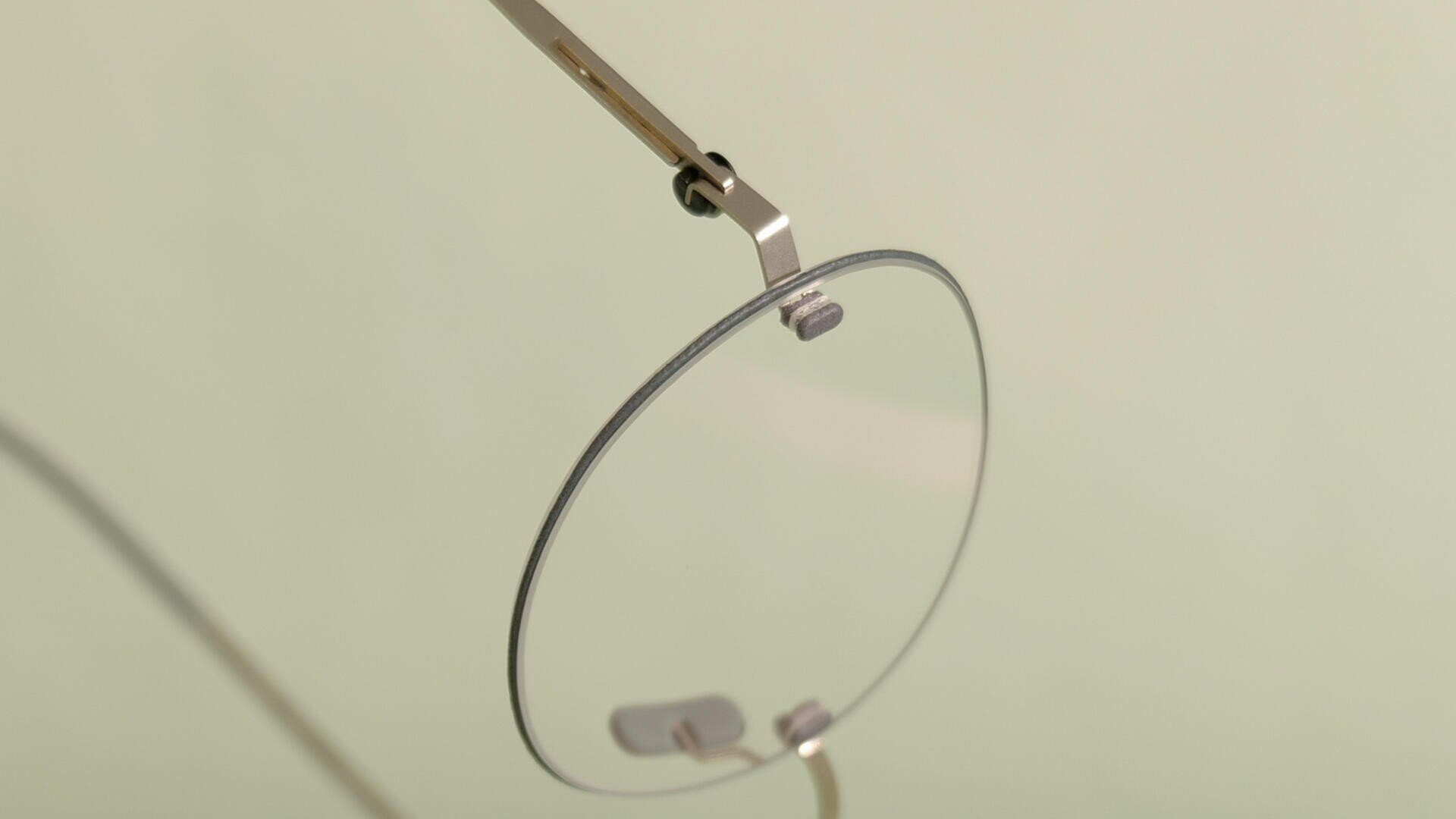 Eine Nahaufnahme eines minimalistischen Brillengestells mit dünnem Metallrand und klaren Gläsern vor einem sanften beigen Hintergrund.