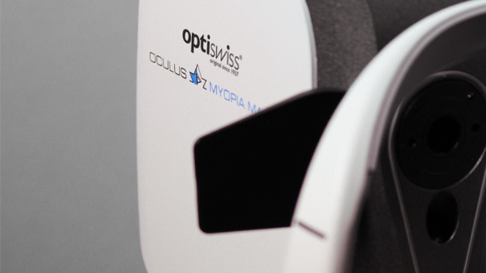 Close-up of an optometric device labeled optiswiss and OCULUS MYOPIA MASTER, used for eye examinations, with a white and black exterior against a neutral background.