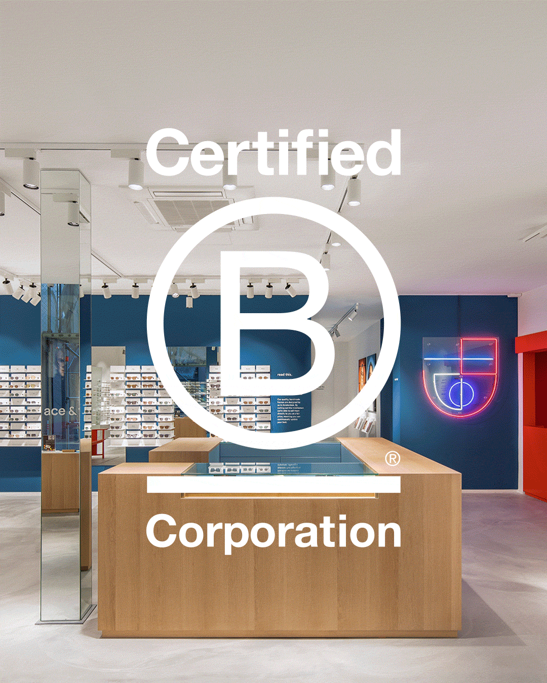 A modern retail store with wooden counters, blue walls and a neon sign emblazoned with the Certified B Corporation logo in white.