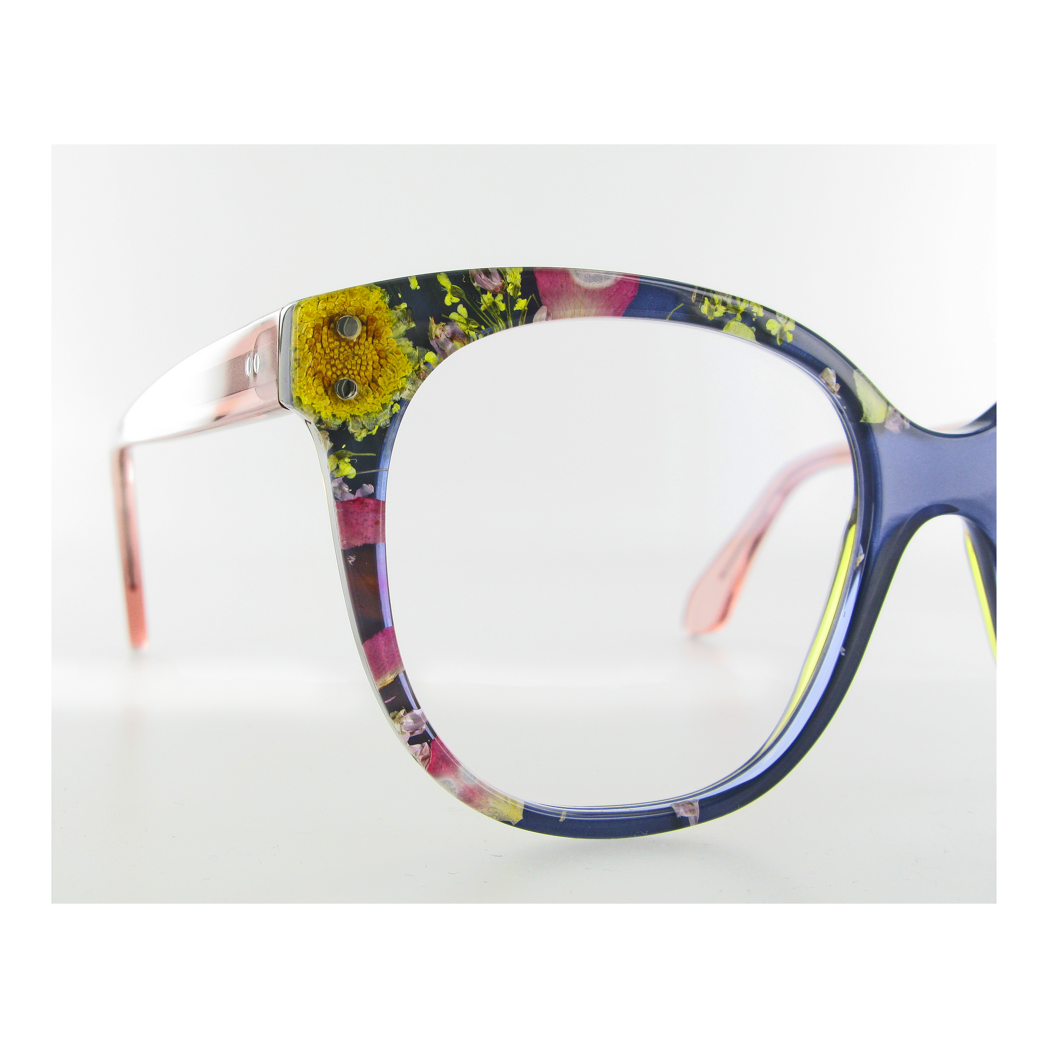 Close-up of eyeglass frames with a transparent section containing embedded dried flowers and greenery, set against a white background.