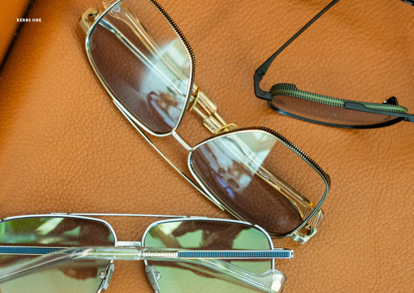 Three pairs of eyeglasses with metal frames rest on a textured brown leather surface. Each pair has a unique frame design, and the lenses reflect the surroundings.